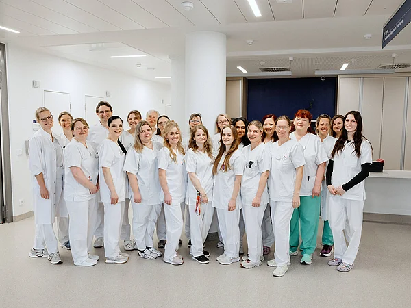 Eine Gruppe von 20 medizinischen Fachkräften in weißen Arbeitskleidungen steht in einem Krankenhausflur und posiert für ein Gruppenfoto.