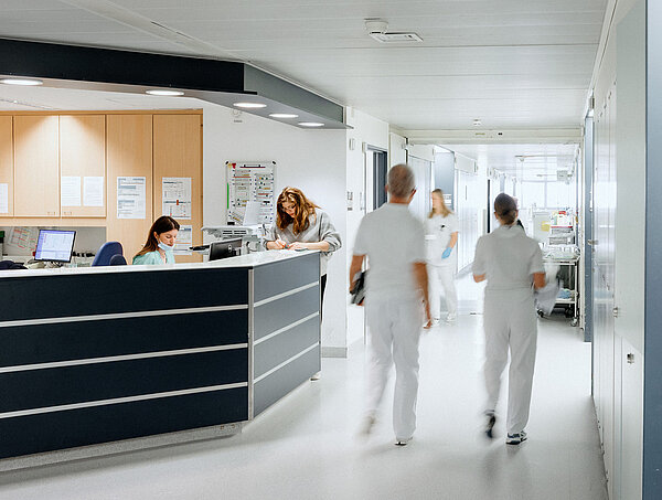 Zwei Pflegekräfte gehen durch einen hellen Krankenhausflur.