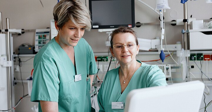 Zwei Pflegekräfte vor Monitor einer Intensivstation im Gespräch über Patientenzustand