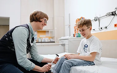 Mitarbeiterin spricht mit einem Kind auf einem Krankenhausbett.